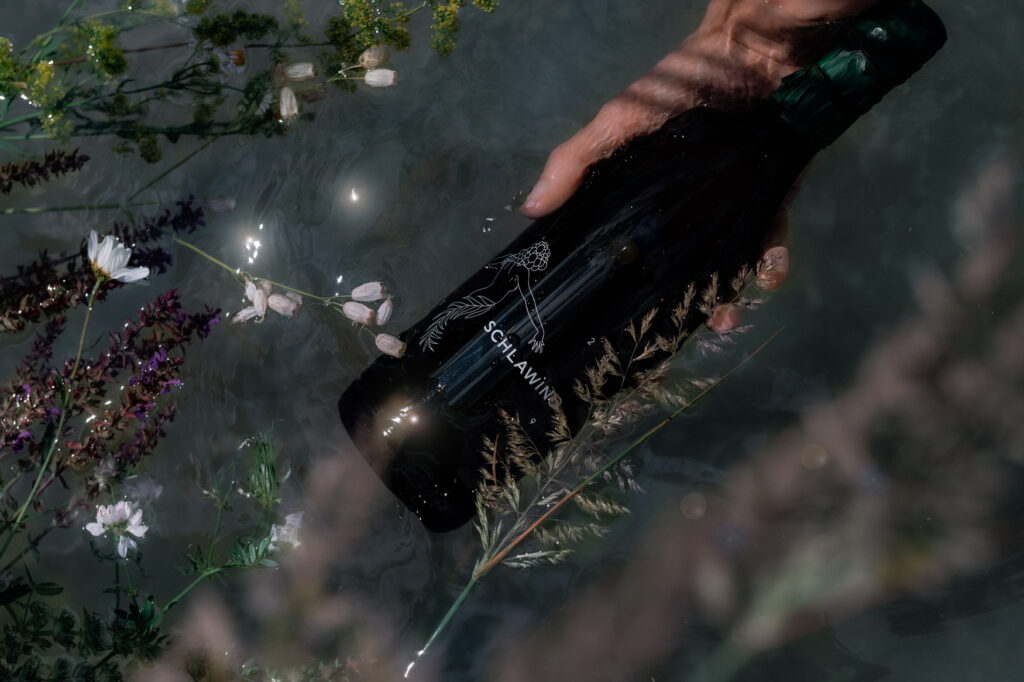 Hand legt eine Flasche Schlawino zwischen Wiesenblumen